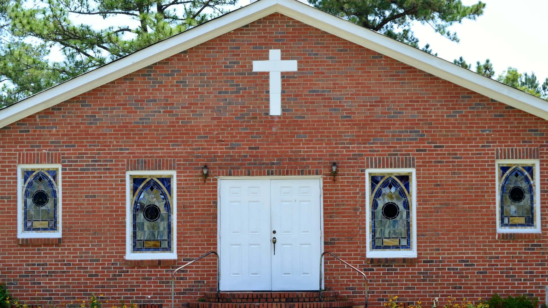 Brick church with a white cross and stained glass windows