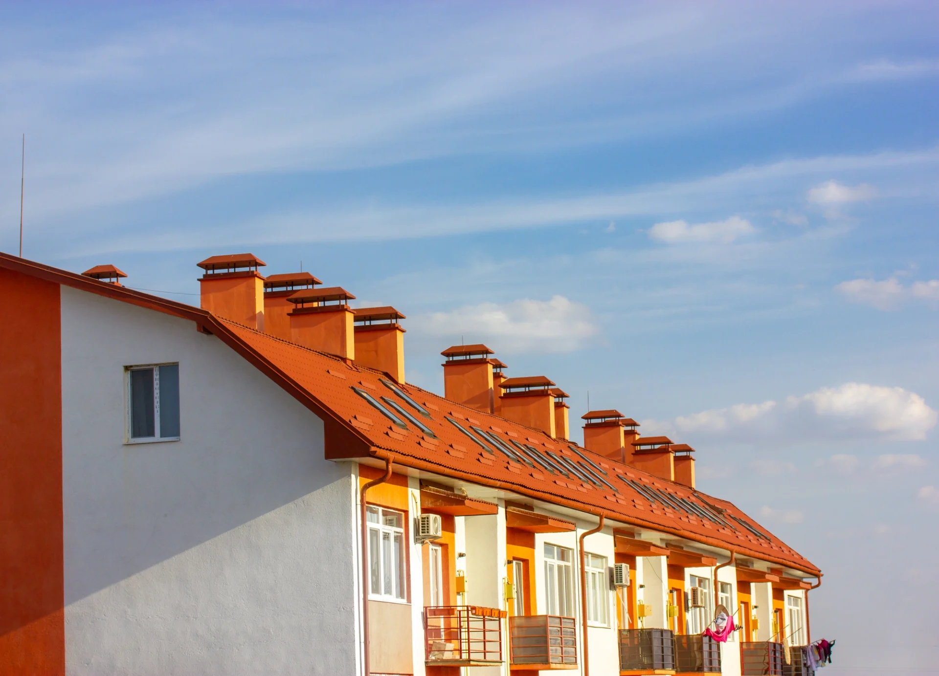 Large red and white apartment building with red terracotta roof shingles against blue sky