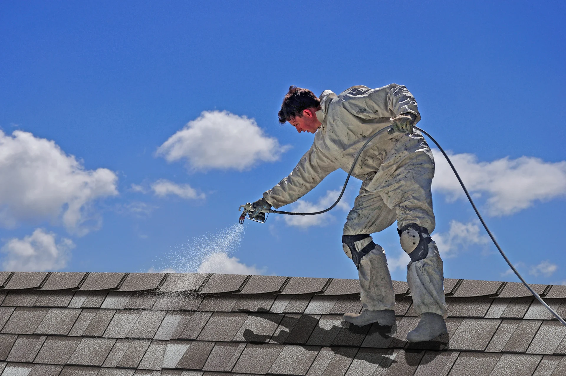 A roofer applying a coating system to a shingle roof.