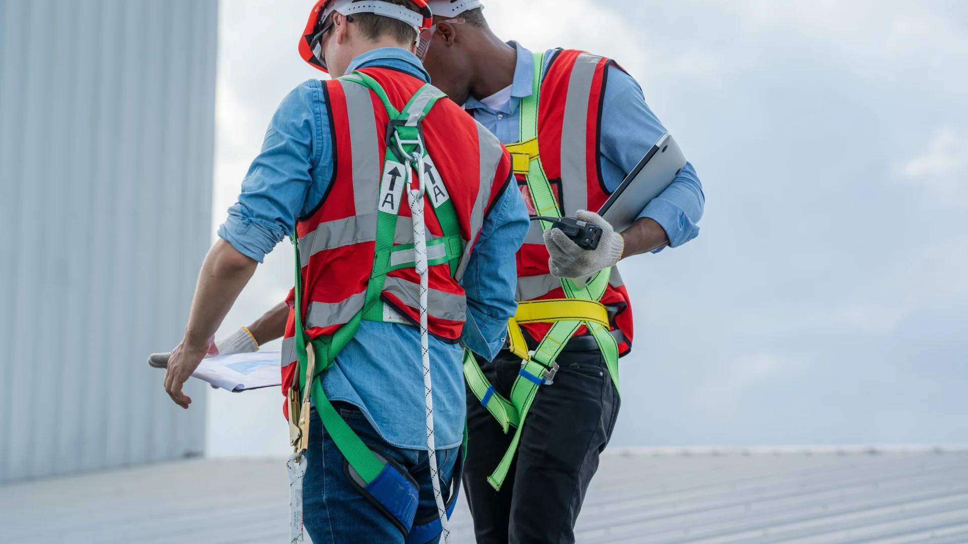 Close view of two roofing contractors in safety gear going over plans while standing on a commercial roof