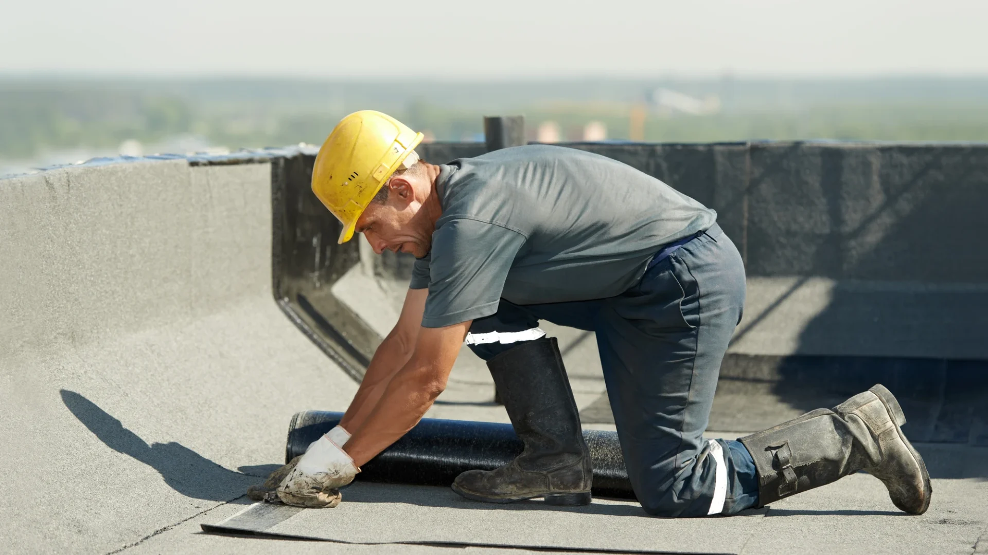 A kneeling roofer applying material to the roof of a commercial building