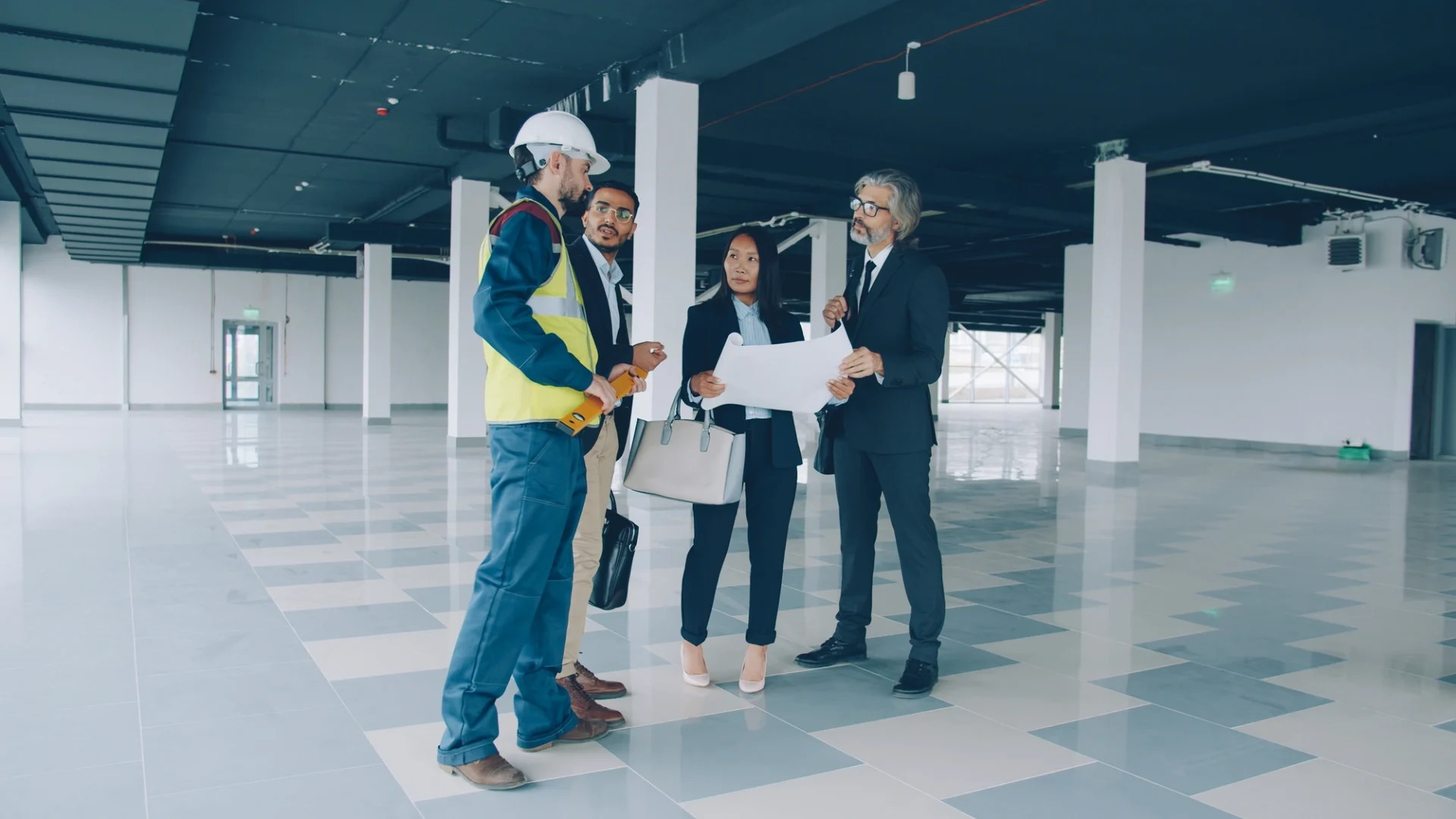 A professional in a hard hat consulting with a management team inside an empty commercial space