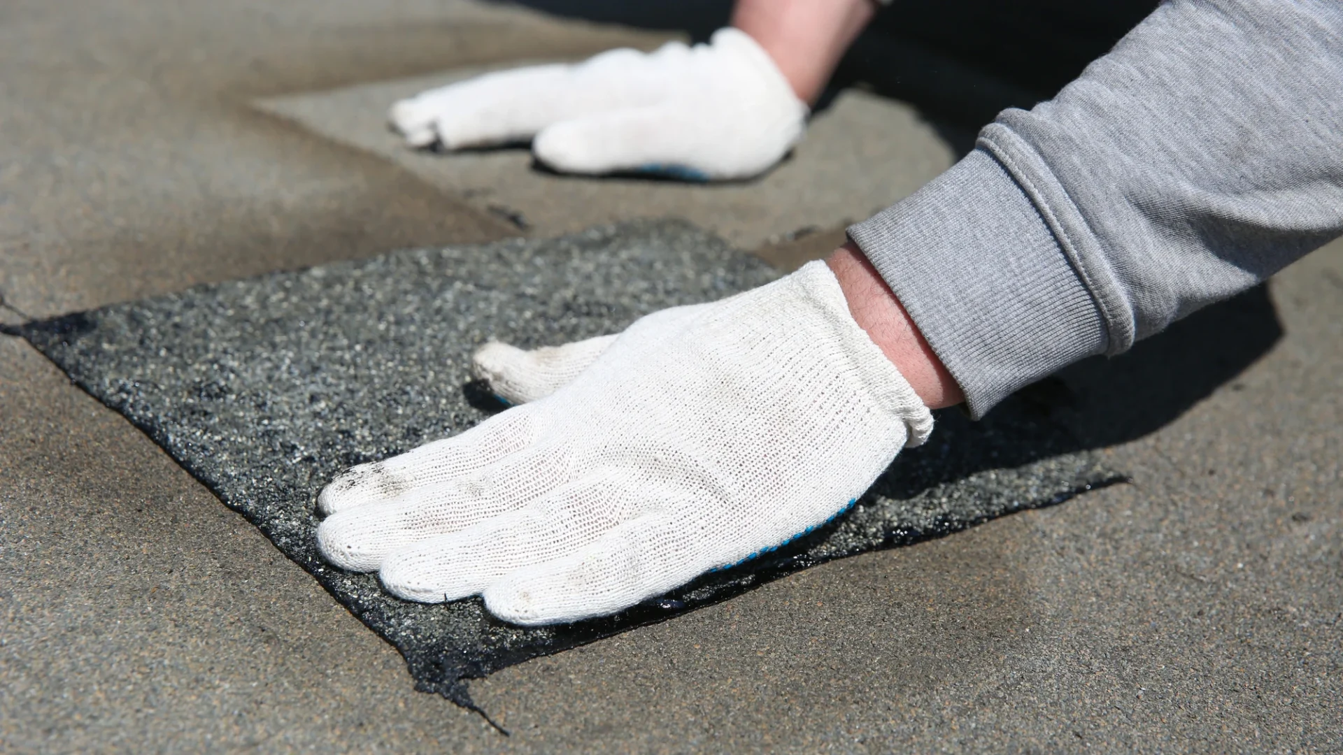 Close view of a roofer placing an asphalt patch on a commercial building with a flat roof