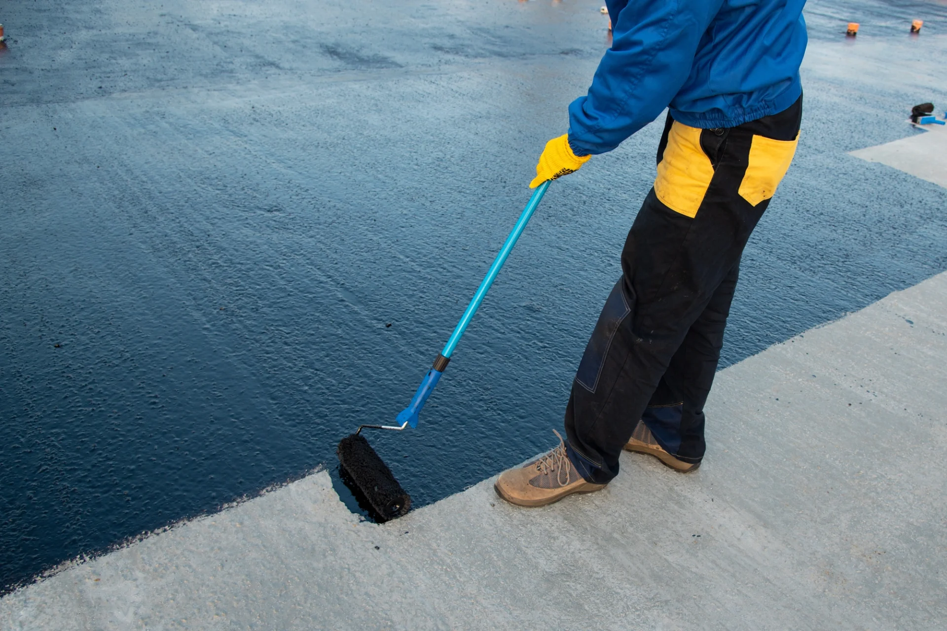 A man is applying a flat roof coating to a roof