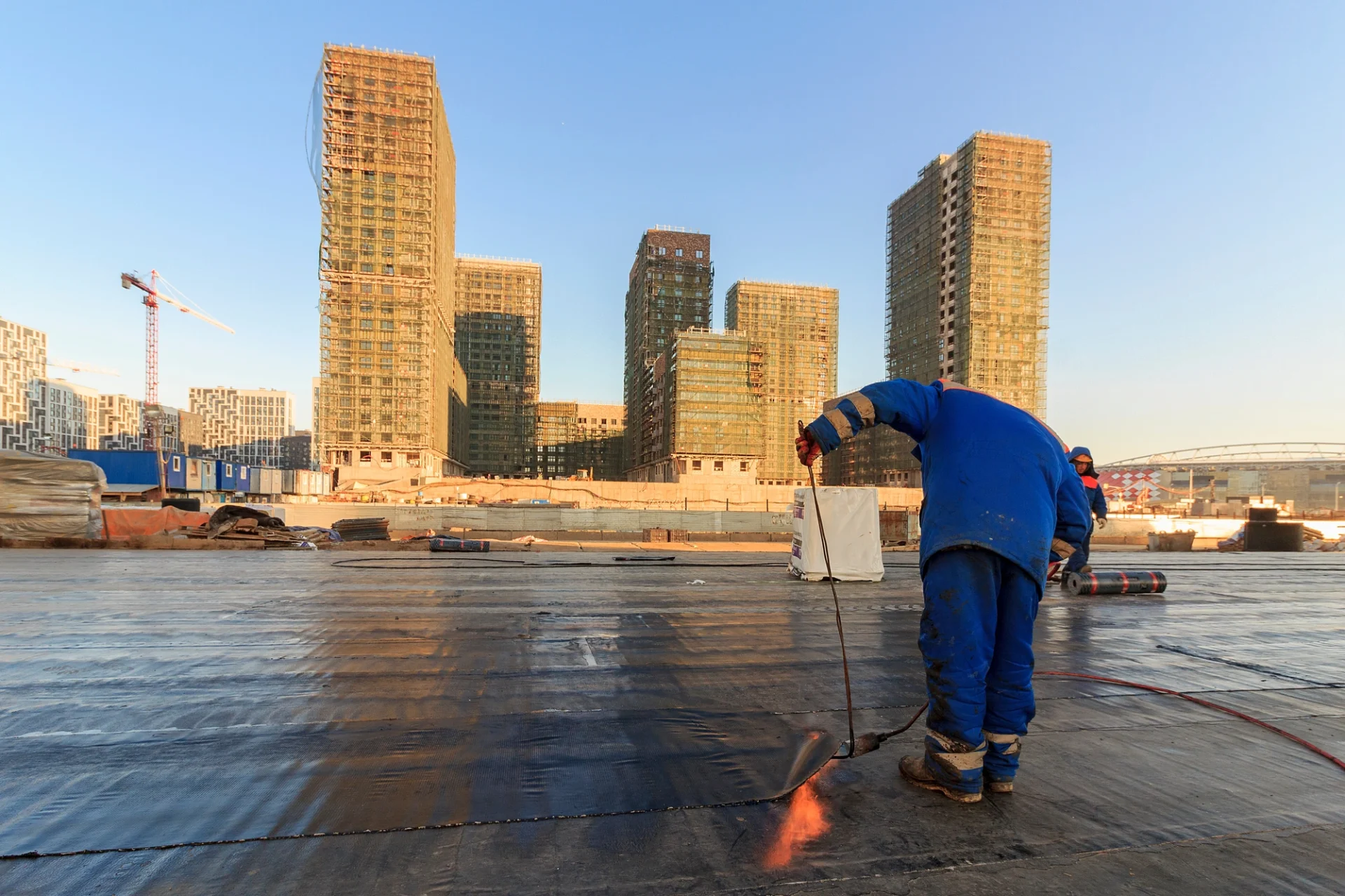 Contractors in protective gear applying a coating to a commercial flat roof