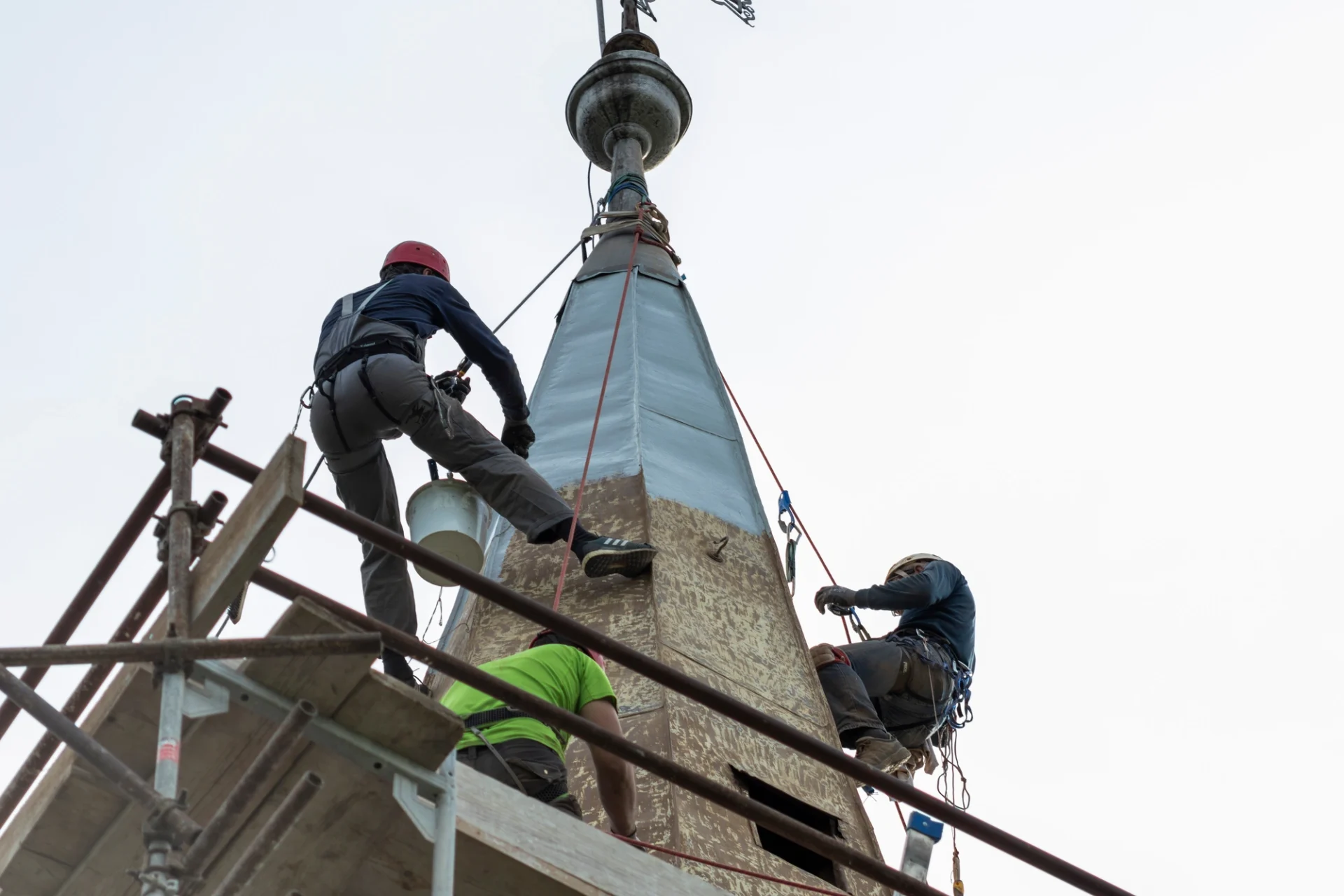 Contractors in harnesses with safety lines restoring a steeple