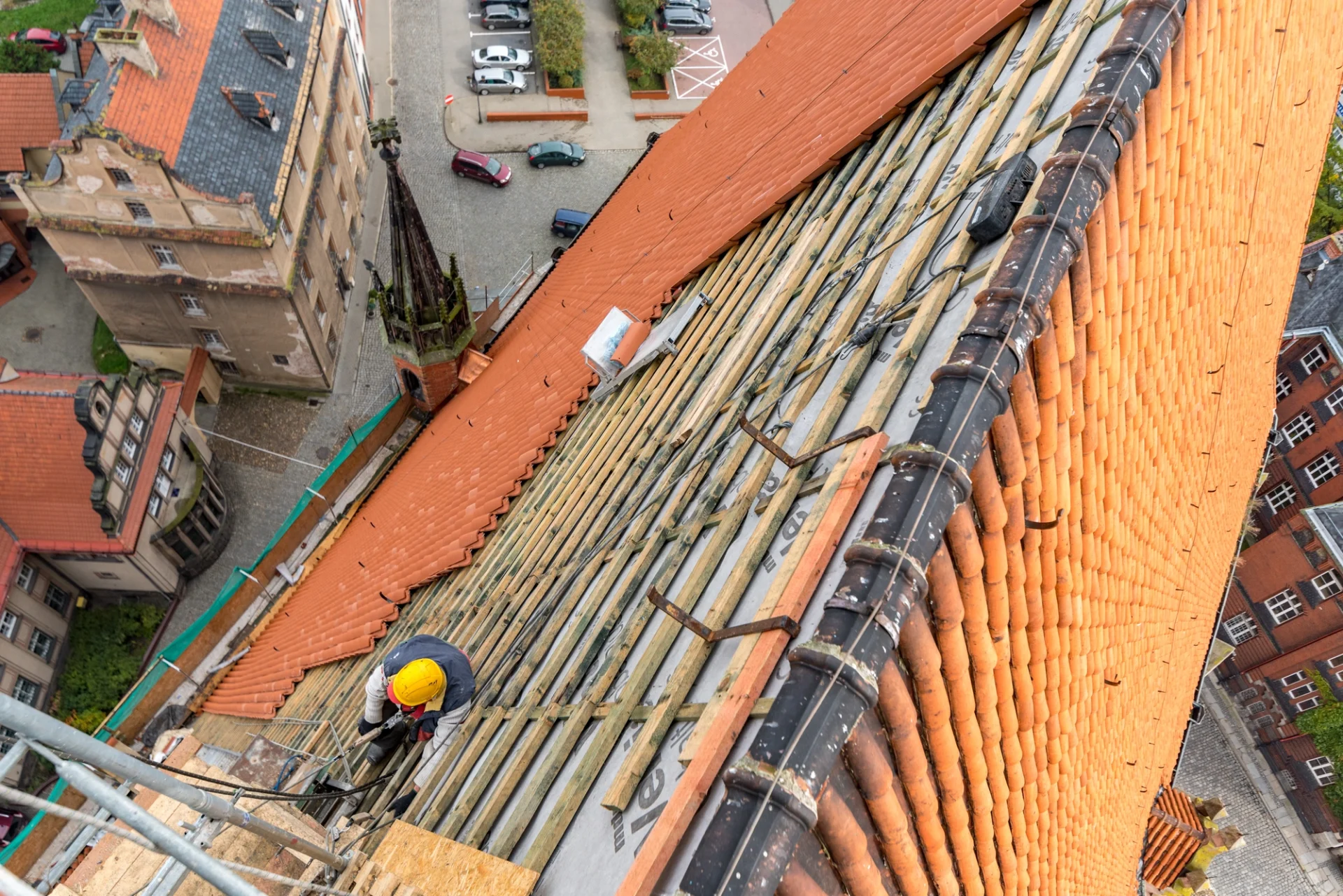 A roofing contractor replacing shingles on a church roof with steep sides