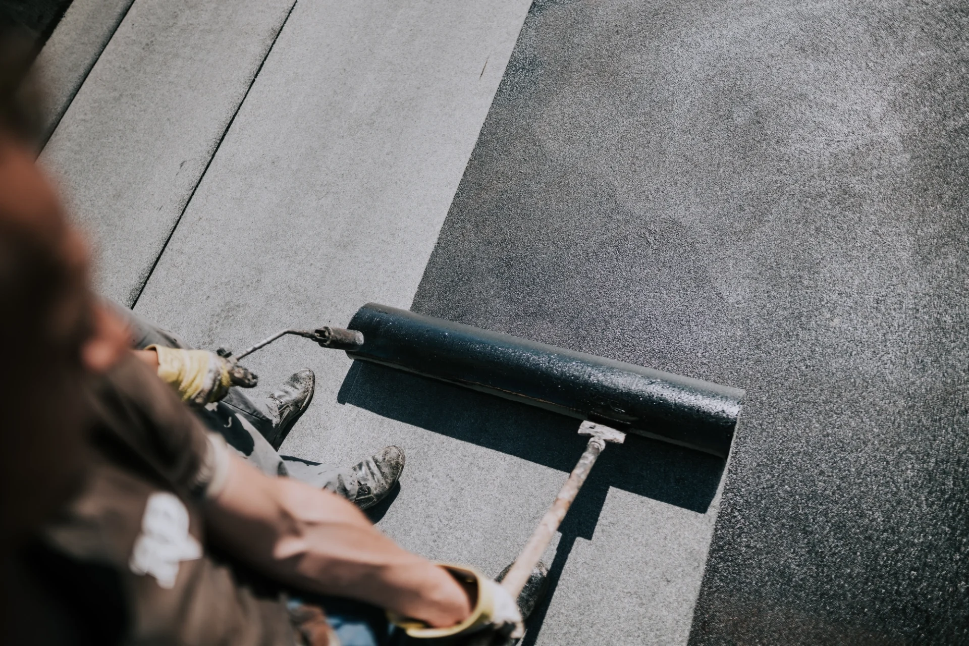 A black coating is being applied to a flat roof
