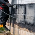 A contractor applying waterproof coating to the exterior of a building’s foundation