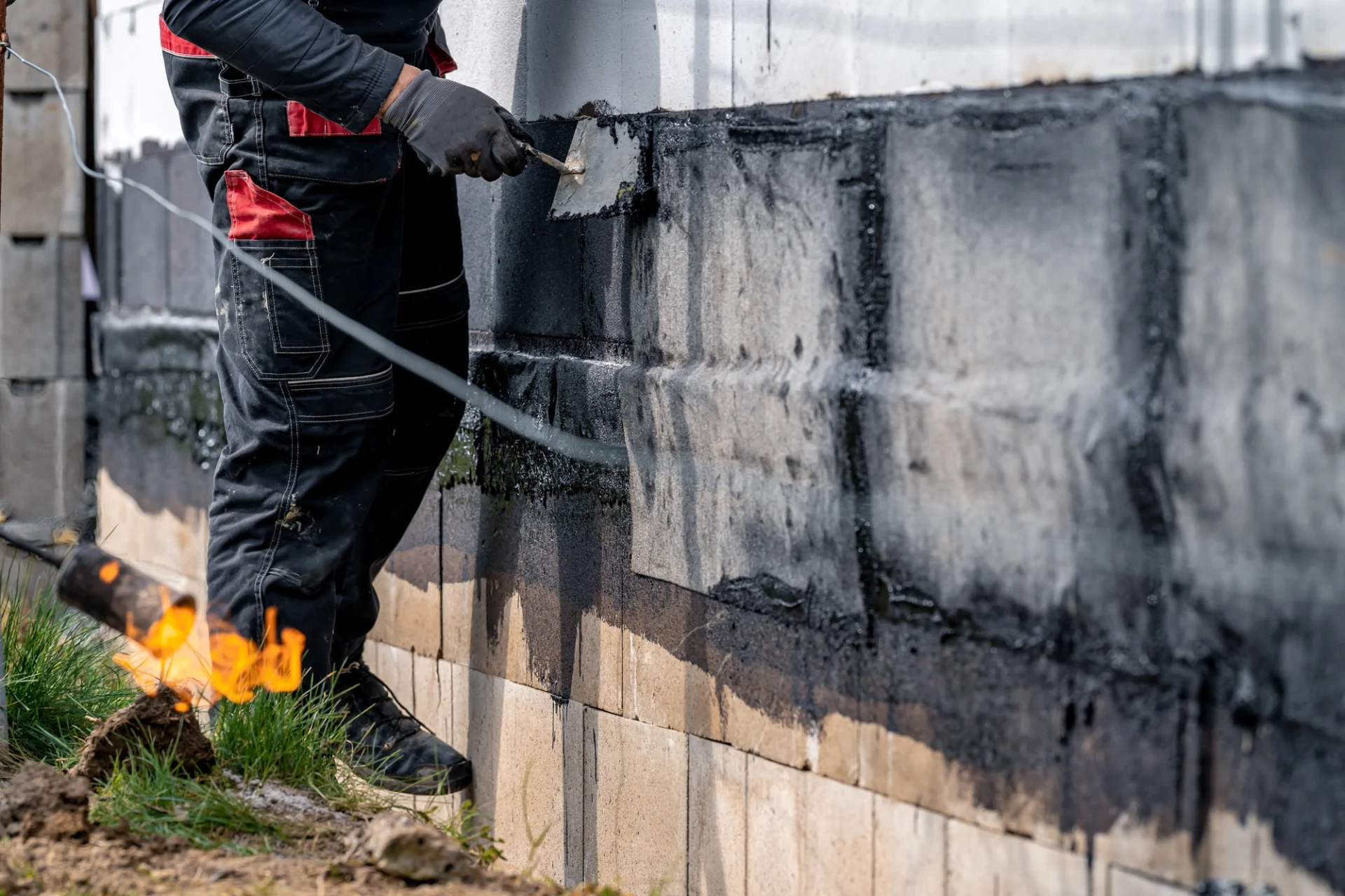 A contractor applying waterproof coating to the exterior of a building’s foundation